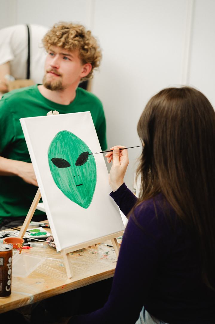 Besucherin malt ein grünes Alien auf Leinwand